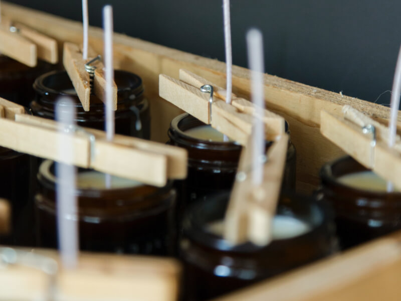 Clothes pins holding wicks in jars filled with wax.
